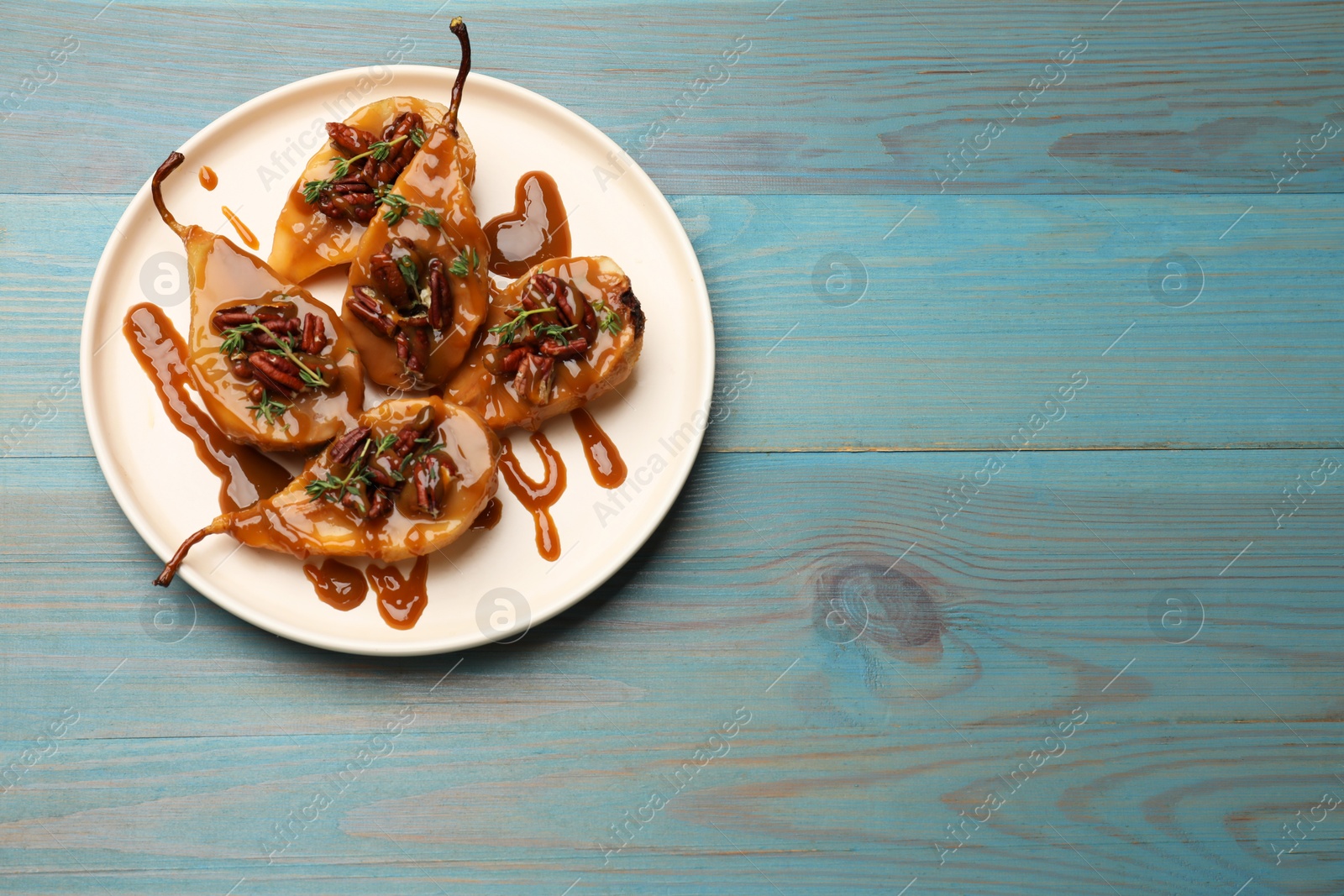 Photo of Delicious pears with caramel sauce, pecan nuts and thyme on light blue wooden table, top view. Space for text