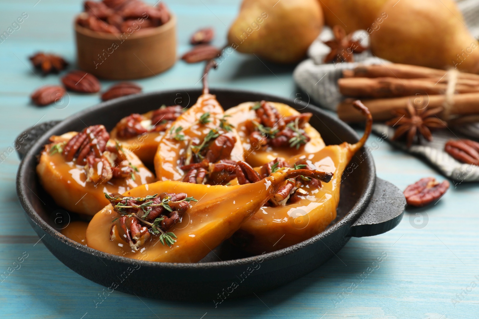 Photo of Delicious pears with caramel sauce, pecan nuts and thyme on light blue wooden table, closeup