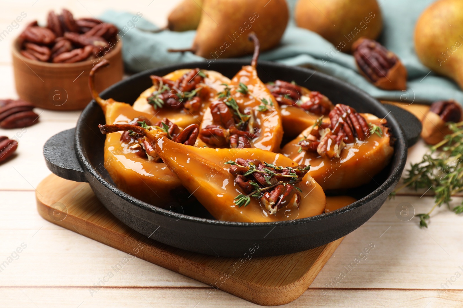 Photo of Delicious pears with caramel sauce, pecan nuts and thyme on wooden table, closeup