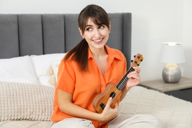 Photo of Happy woman playing ukulele on bed at home