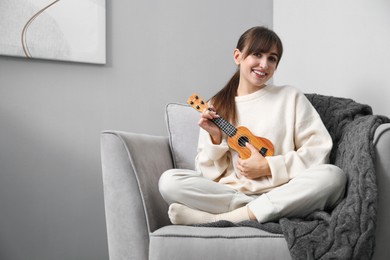 Photo of Happy woman playing ukulele in armchair at home