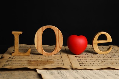 Photo of Word Love made of wooden letters and heart with musical notes on black background