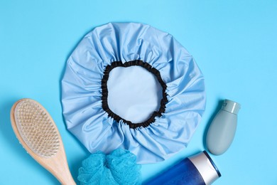 Photo of Shower cap and bath accessories on light blue background, flat lay