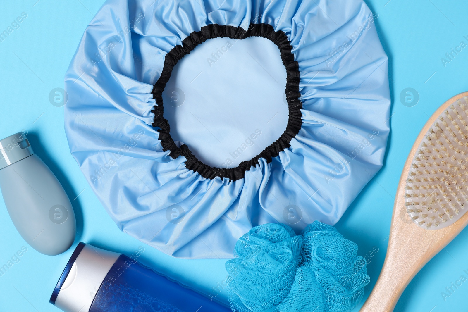 Photo of Shower cap and bath accessories on light blue background, flat lay