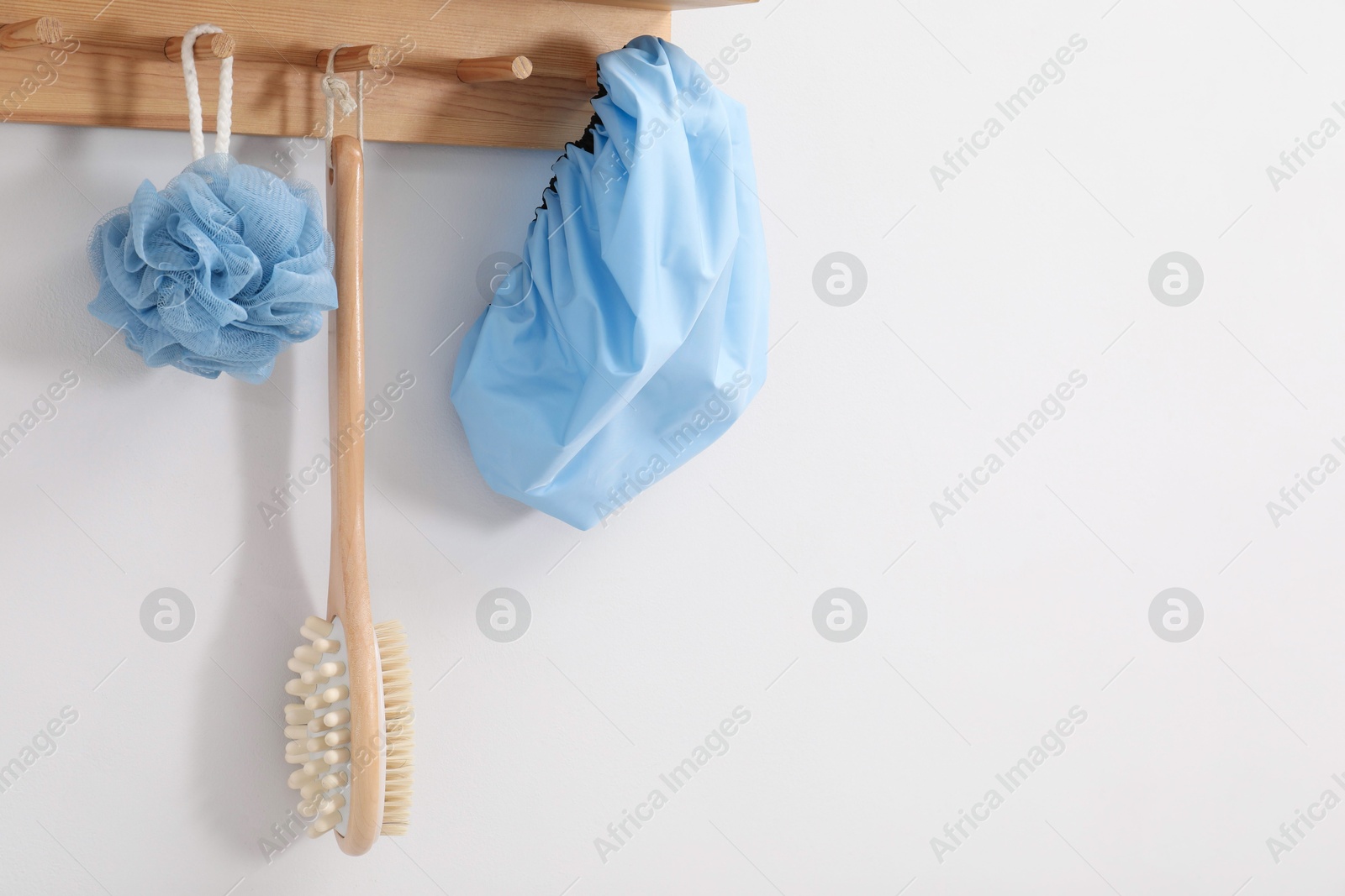 Photo of Shower cap, brush and mesh sponge on rack indoors, space for text