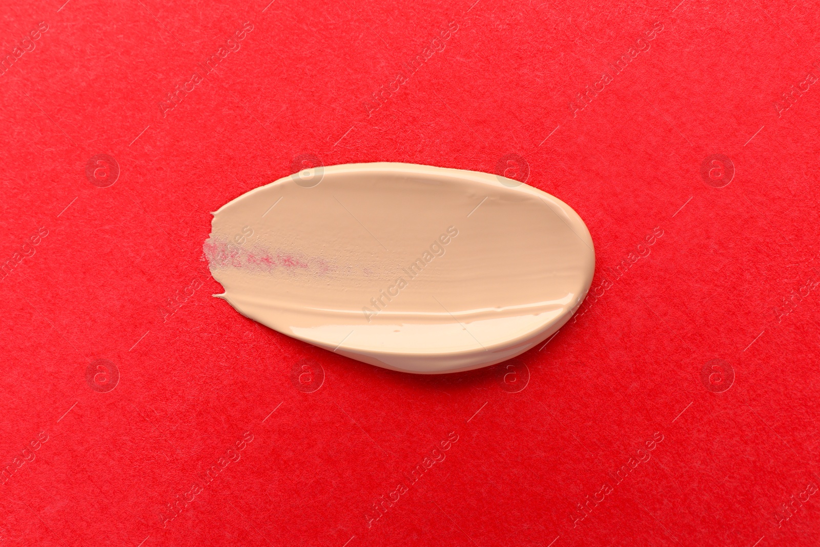 Photo of Smear of foundation on red background, top view