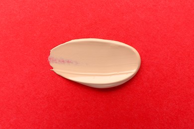 Photo of Smear of foundation on red background, top view