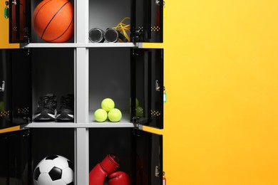 Photo of Open lockers with sport equipment on orange background, space for text