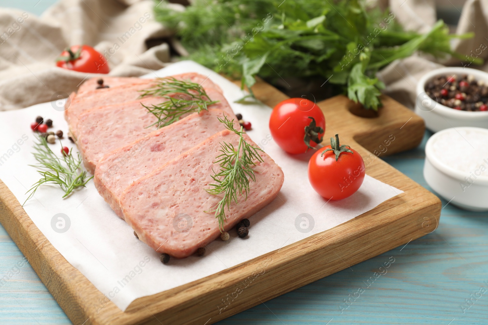 Photo of Pieces of tasty canned meat, dill, peppercorns and tomatoes on light blue wooden table, closeup