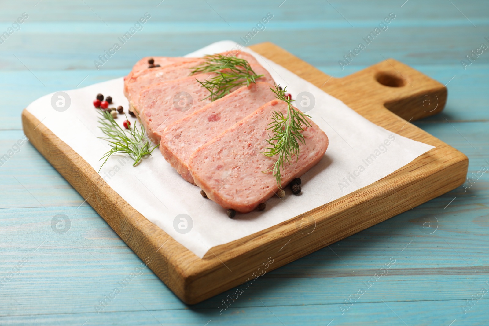 Photo of Pieces of tasty canned meat, dill and peppercorns on light blue wooden table, closeup