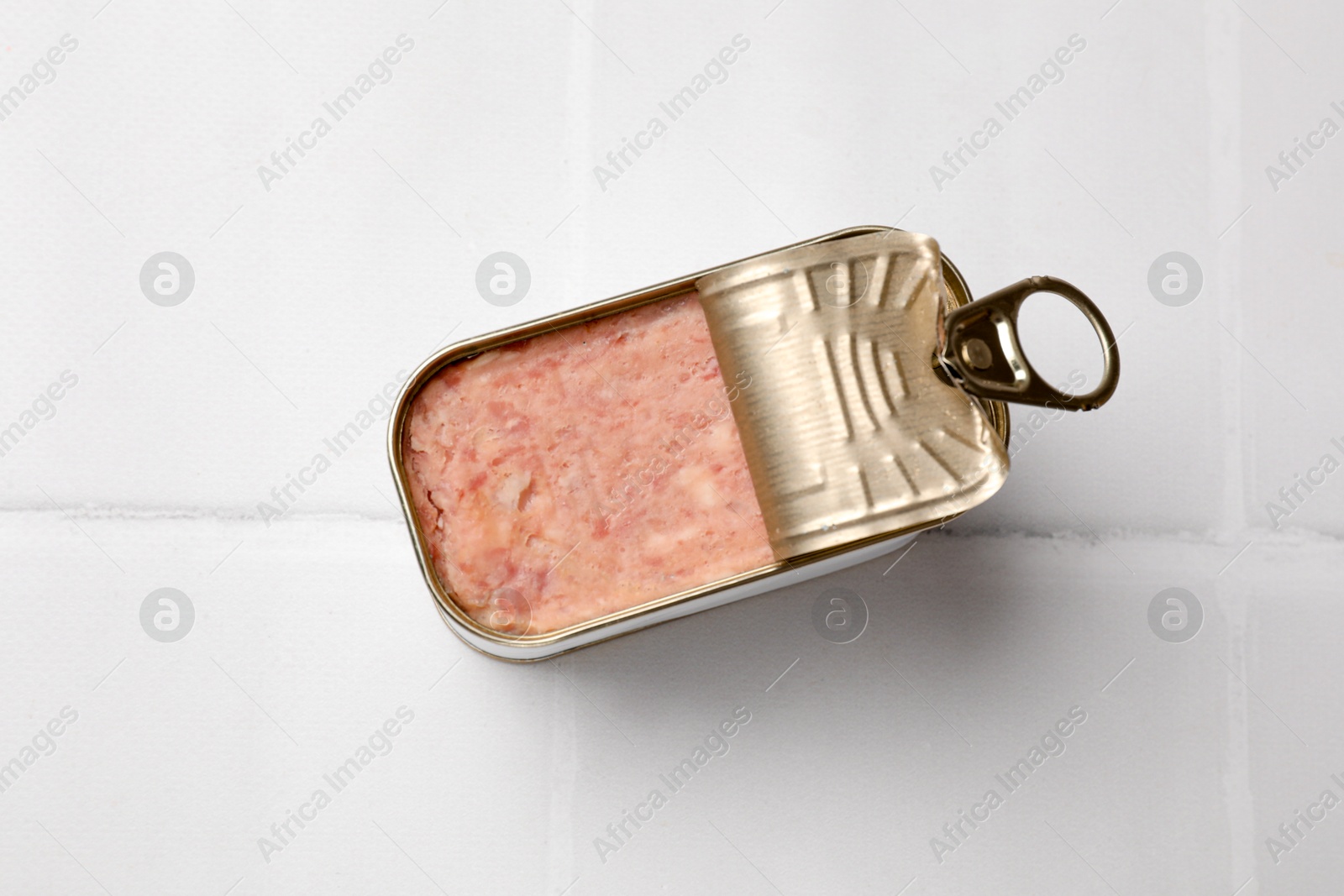 Photo of Tasty canned meat in tin can on white tiled table, top view