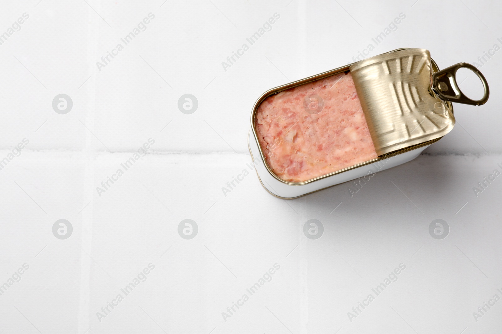 Photo of Tasty canned meat in tin can on white tiled table, top view. Space for text