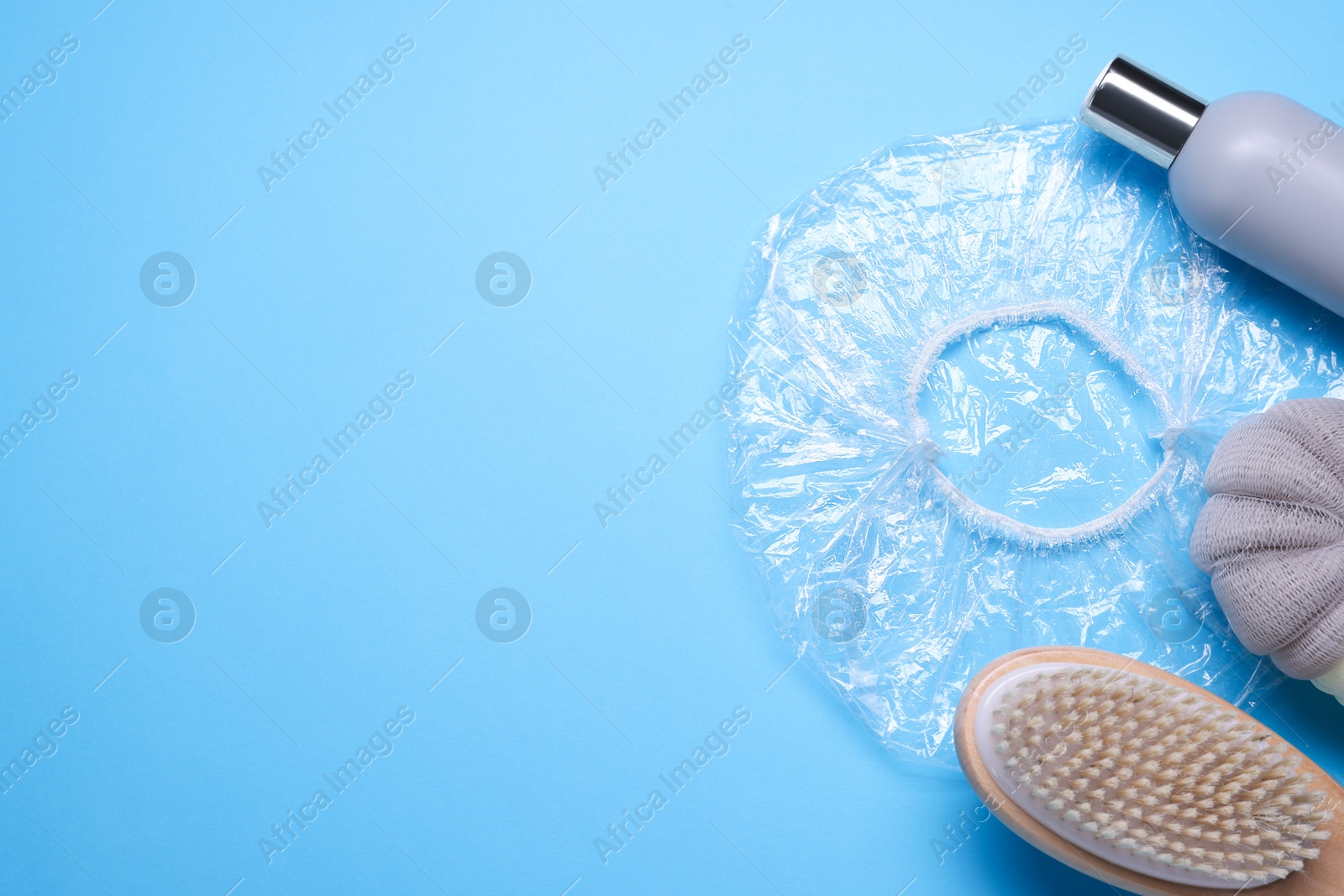 Photo of Shower cap and bath accessories on light blue background, flat lay. Space for text