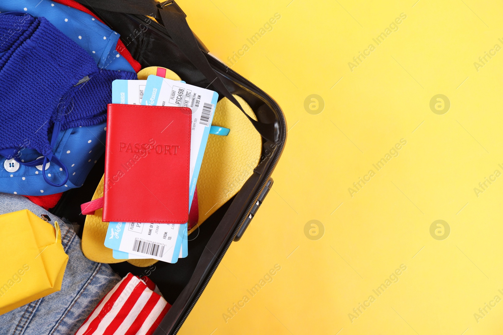 Photo of Travel abroad. Packed suitcase, passport and tickets on yellow background, top view. Space for text