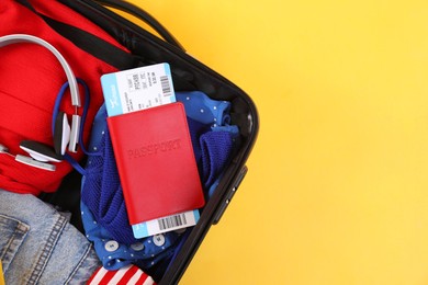 Photo of Travel abroad. Packed suitcase, passport and tickets on yellow background, top view. Space for text