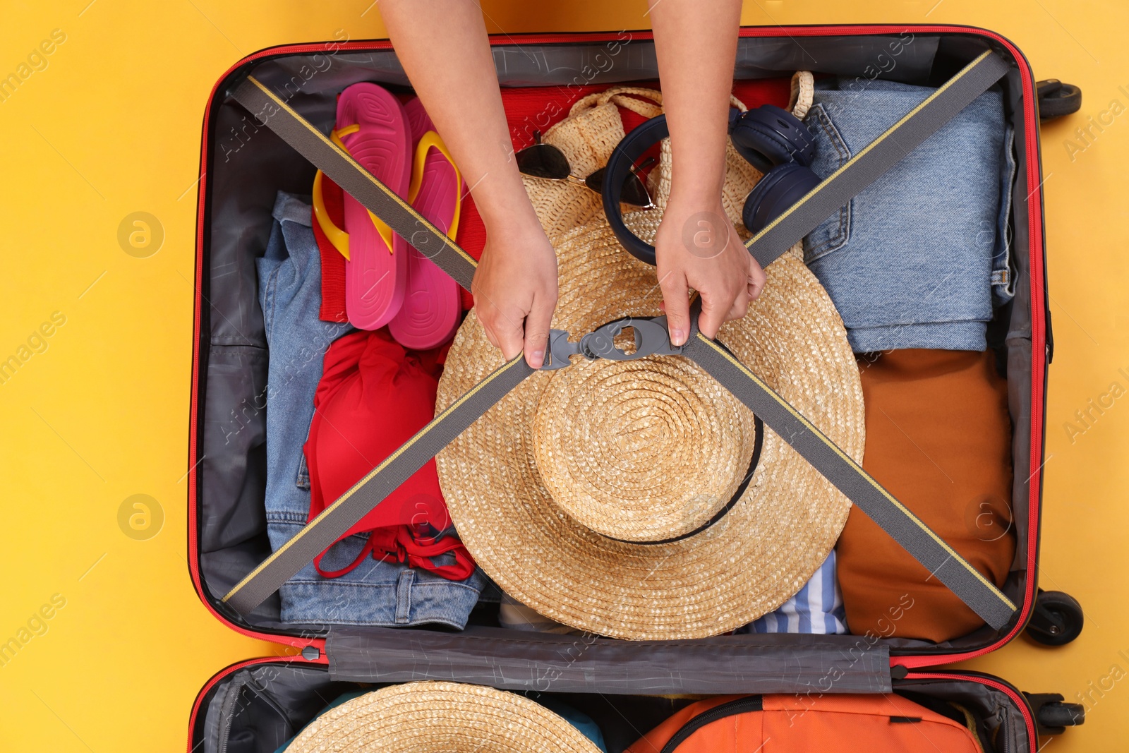 Photo of Traveler packing suitcase on yellow background, top view