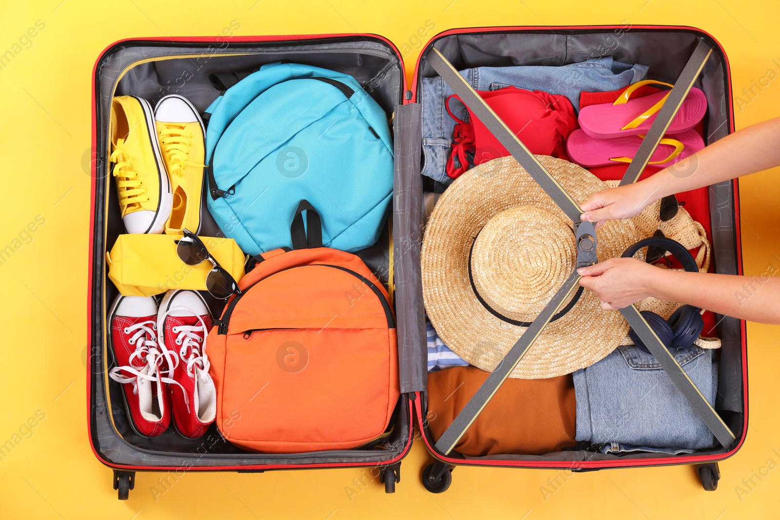 Photo of Traveler packing suitcase on yellow background, top view