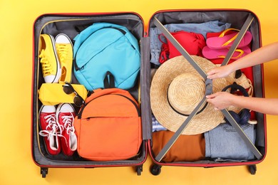 Photo of Traveler packing suitcase on yellow background, top view