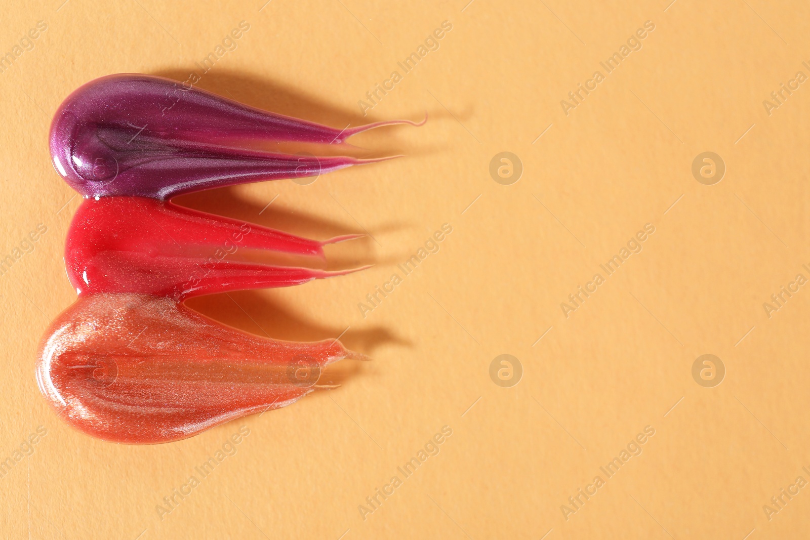 Photo of Samples of different lipglosses on beige background, top view. Space for text