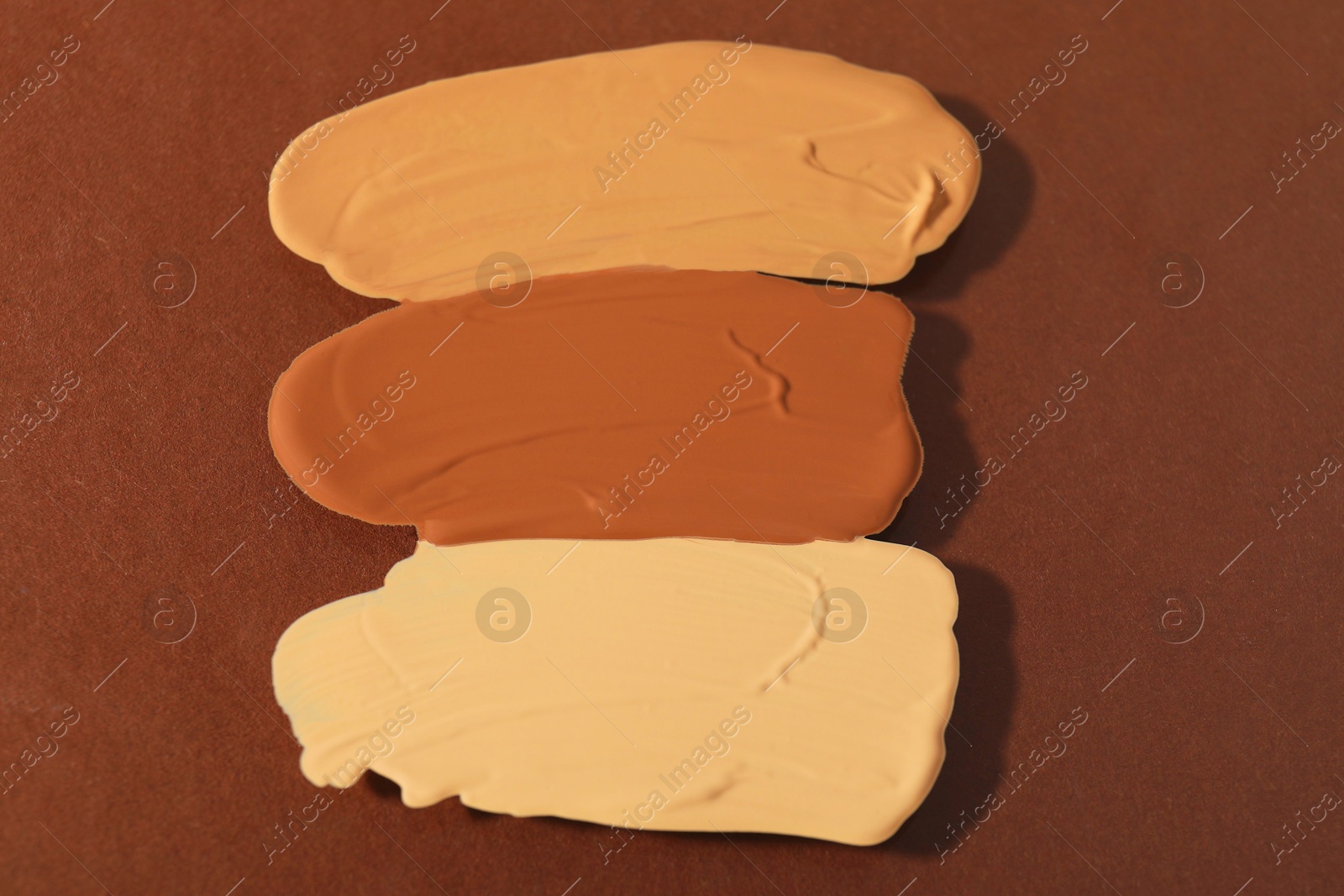 Photo of Samples of different foundations on brown background, closeup