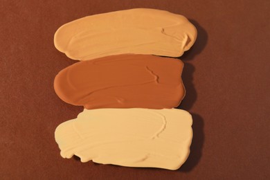 Photo of Samples of different foundations on brown background, closeup