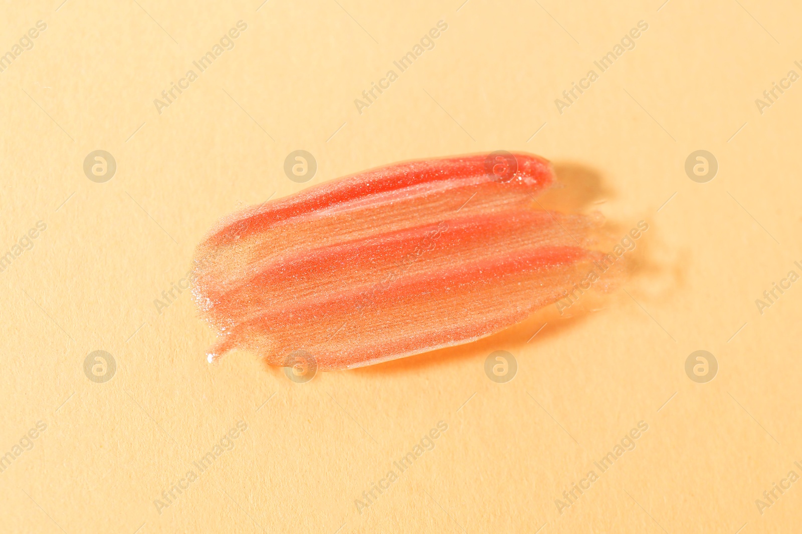 Photo of Sample of orange lipgloss on beige background, closeup