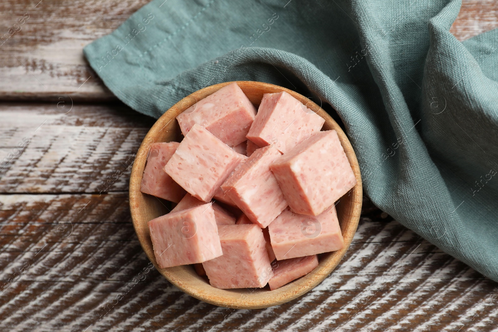 Photo of Pieces of canned meat in bowl and towel on wooden table, top view