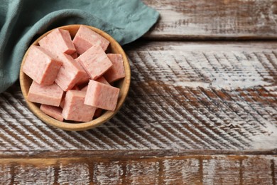 Photo of Pieces of canned meat in bowl and towel on wooden table, top view. Space for text