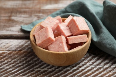 Photo of Pieces of canned meat in bowl and towel on wooden table, closeup