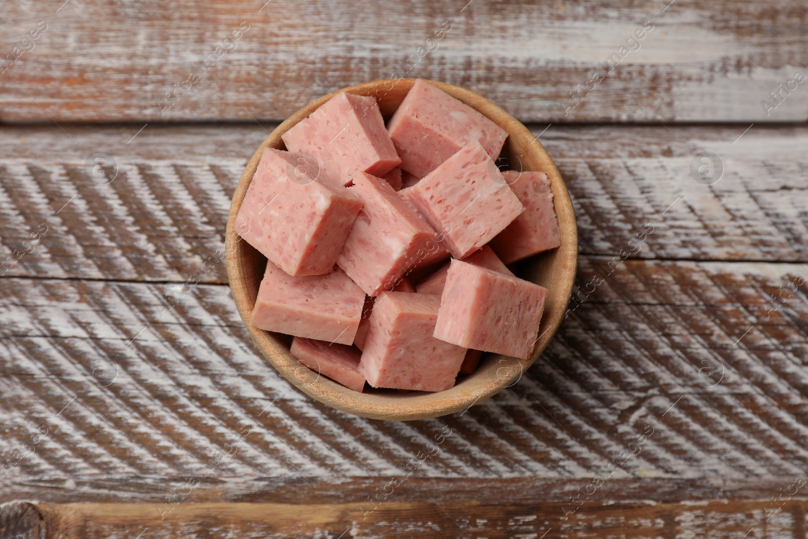 Photo of Pieces of canned meat in bowl on wooden table, top view