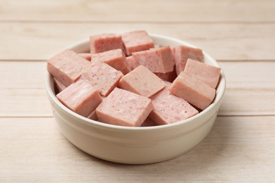 Photo of Pieces of canned meat in bowl on white wooden table, closeup