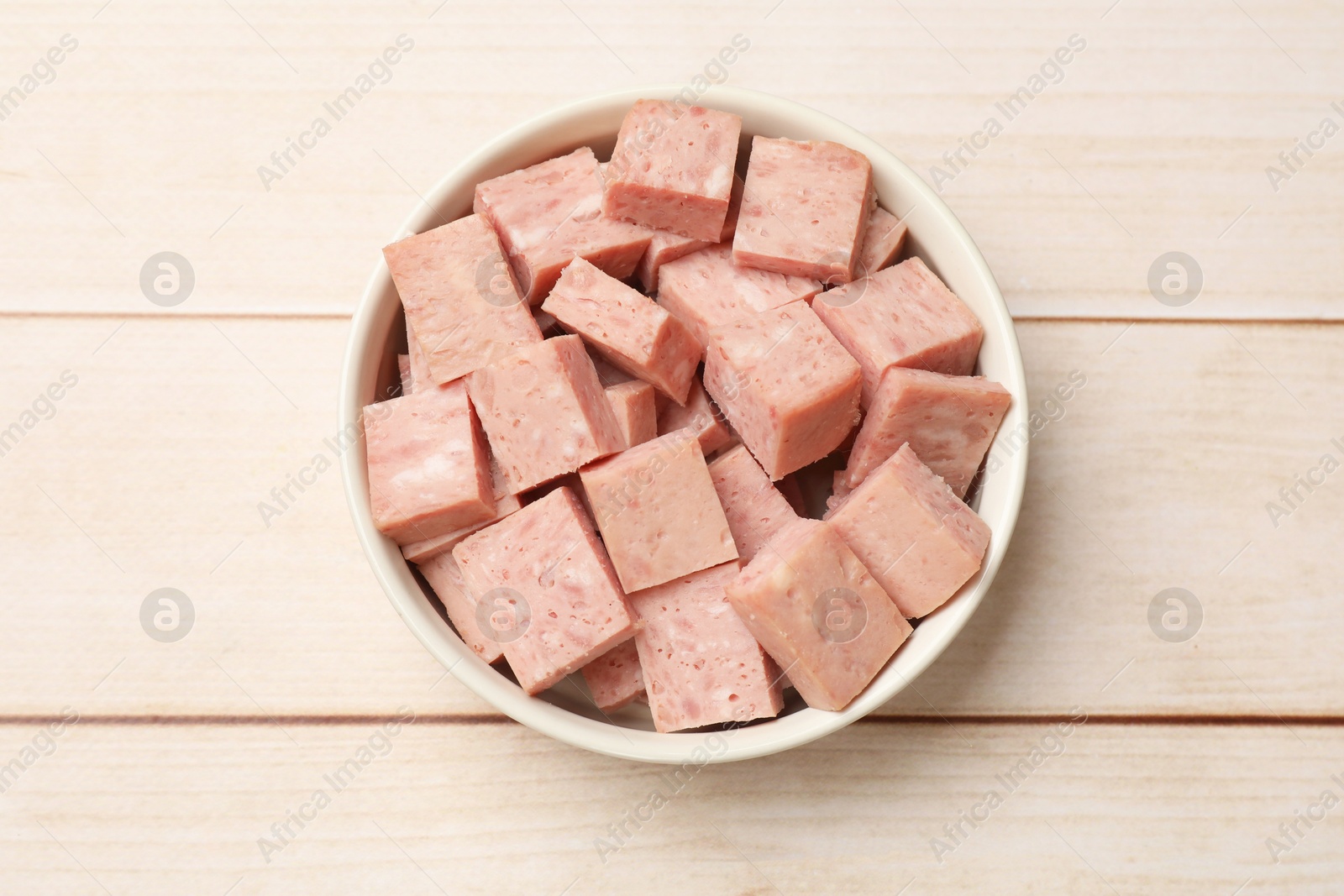 Photo of Pieces of canned meat in bowl on white wooden table, top view