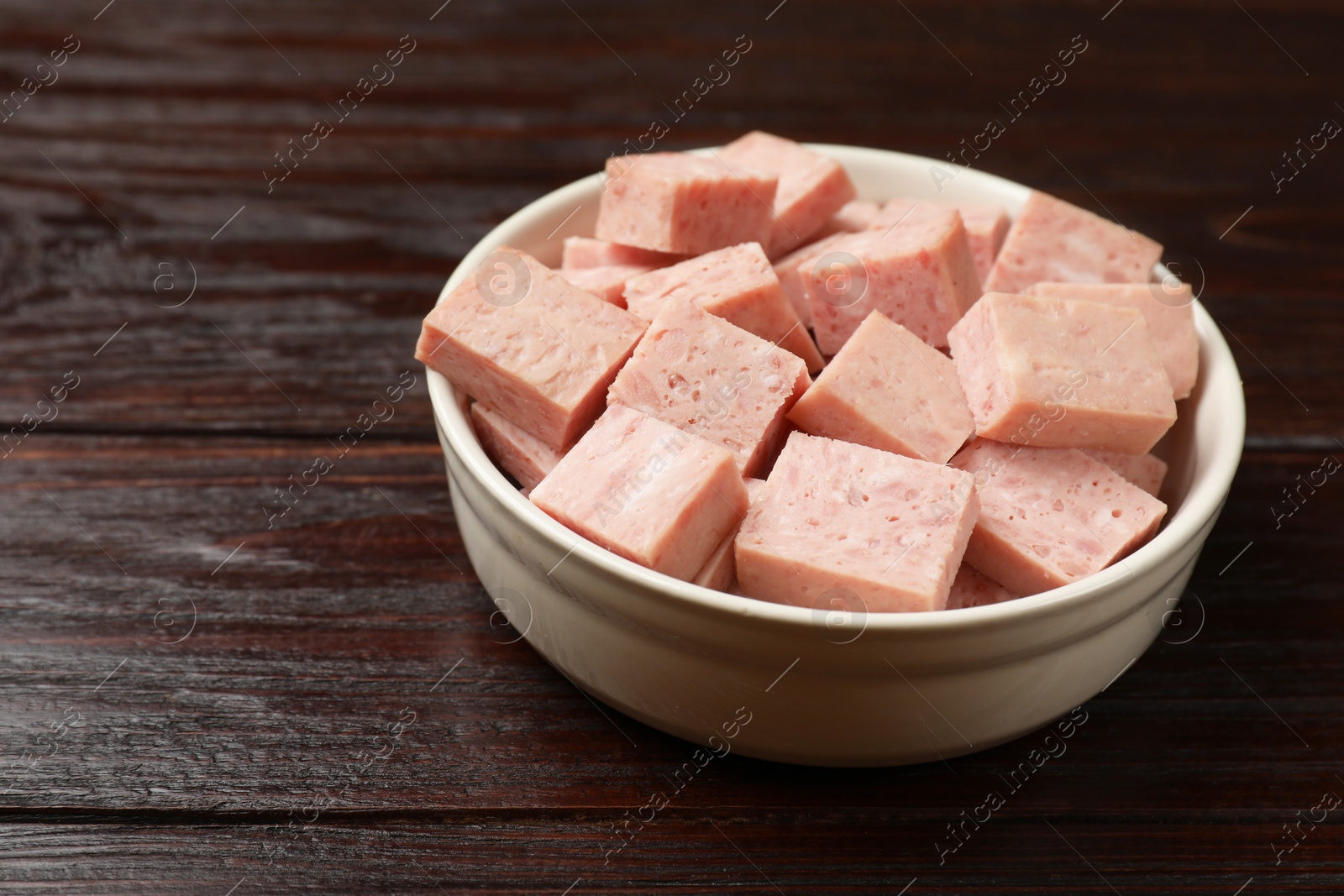 Photo of Pieces of canned meat in bowl on wooden table, closeup