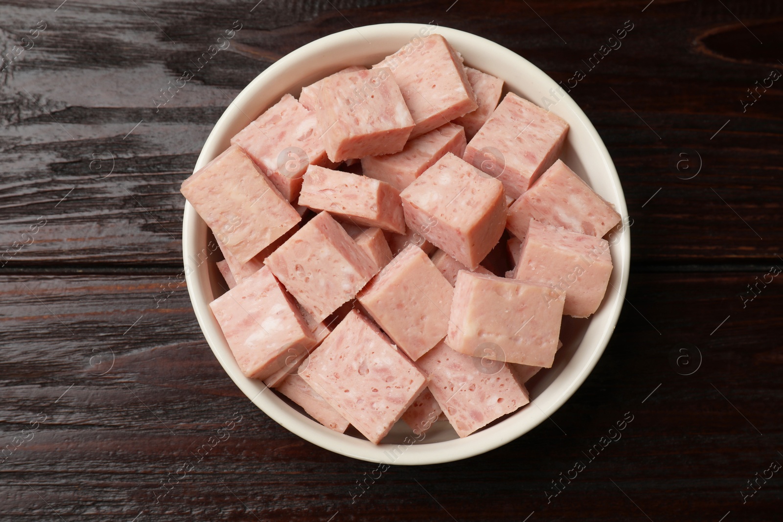 Photo of Pieces of canned meat in bowl on wooden table, top view