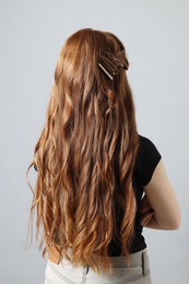 Photo of Teenage girl with stylish hair clips on light grey background, back view