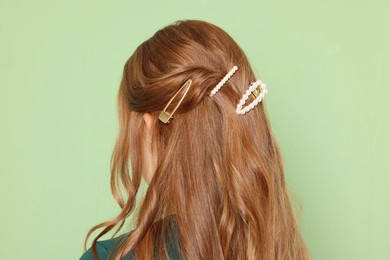 Teenage girl with stylish hair clips on light green background, back view