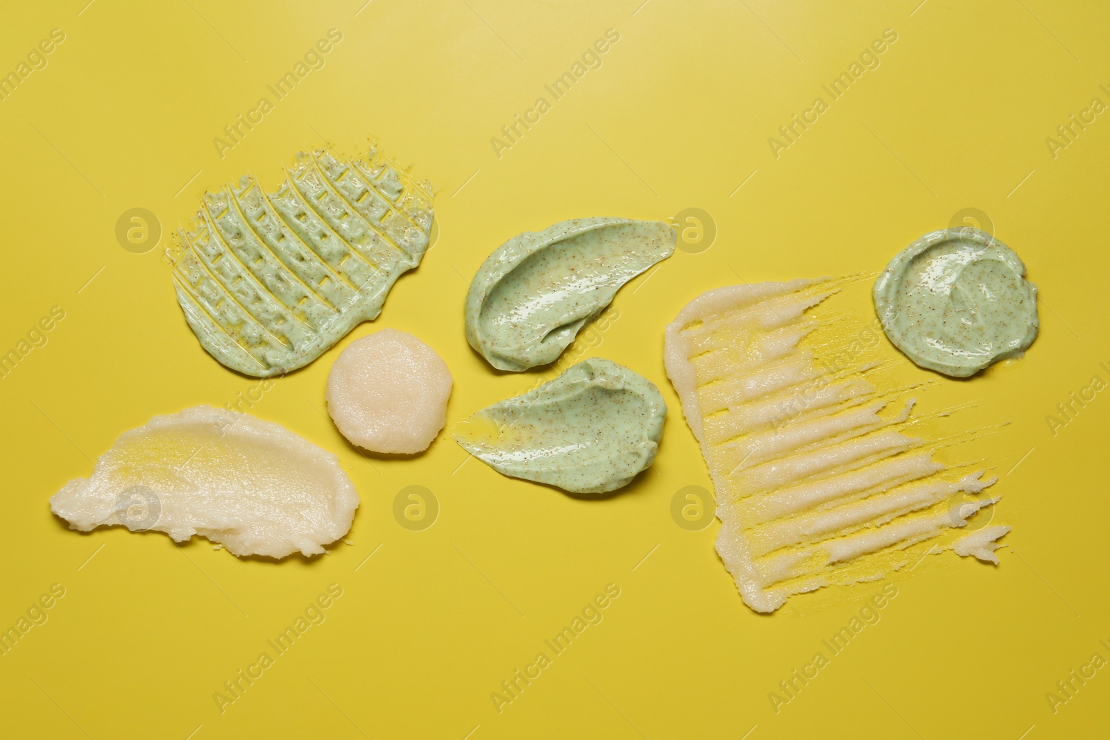 Photo of Samples of different body scrubs on yellow background, top view