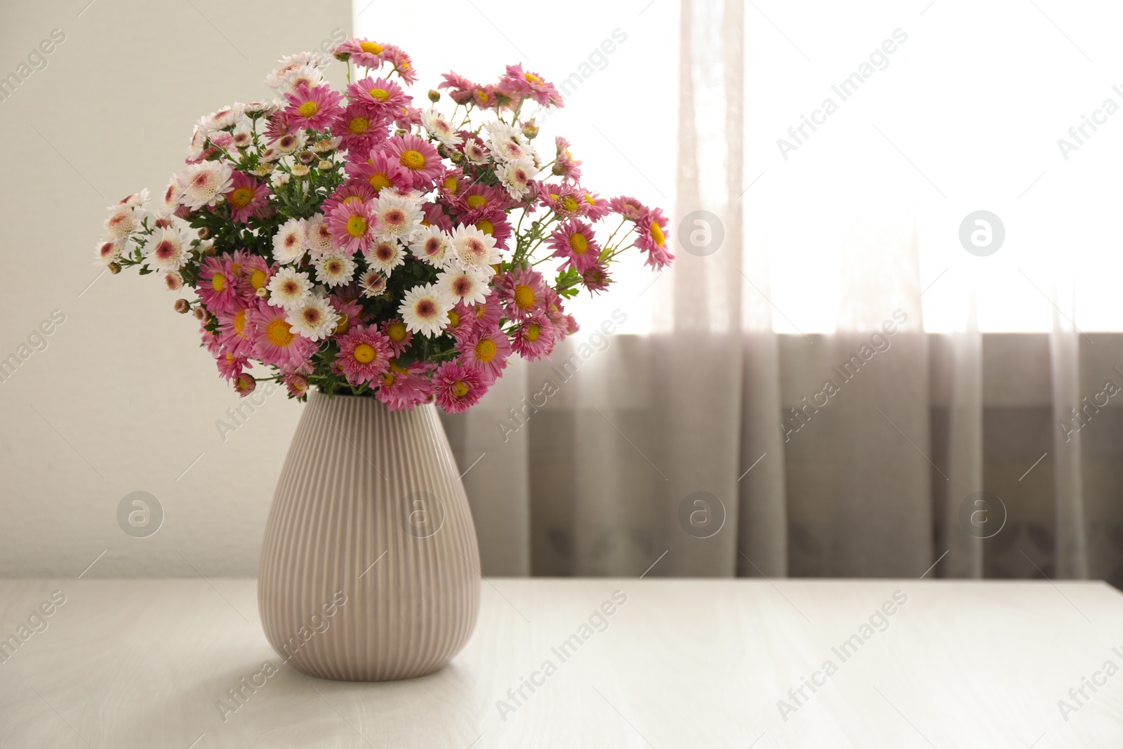 Photo of Beautiful flowers in vase on white wooden table at home, space for text