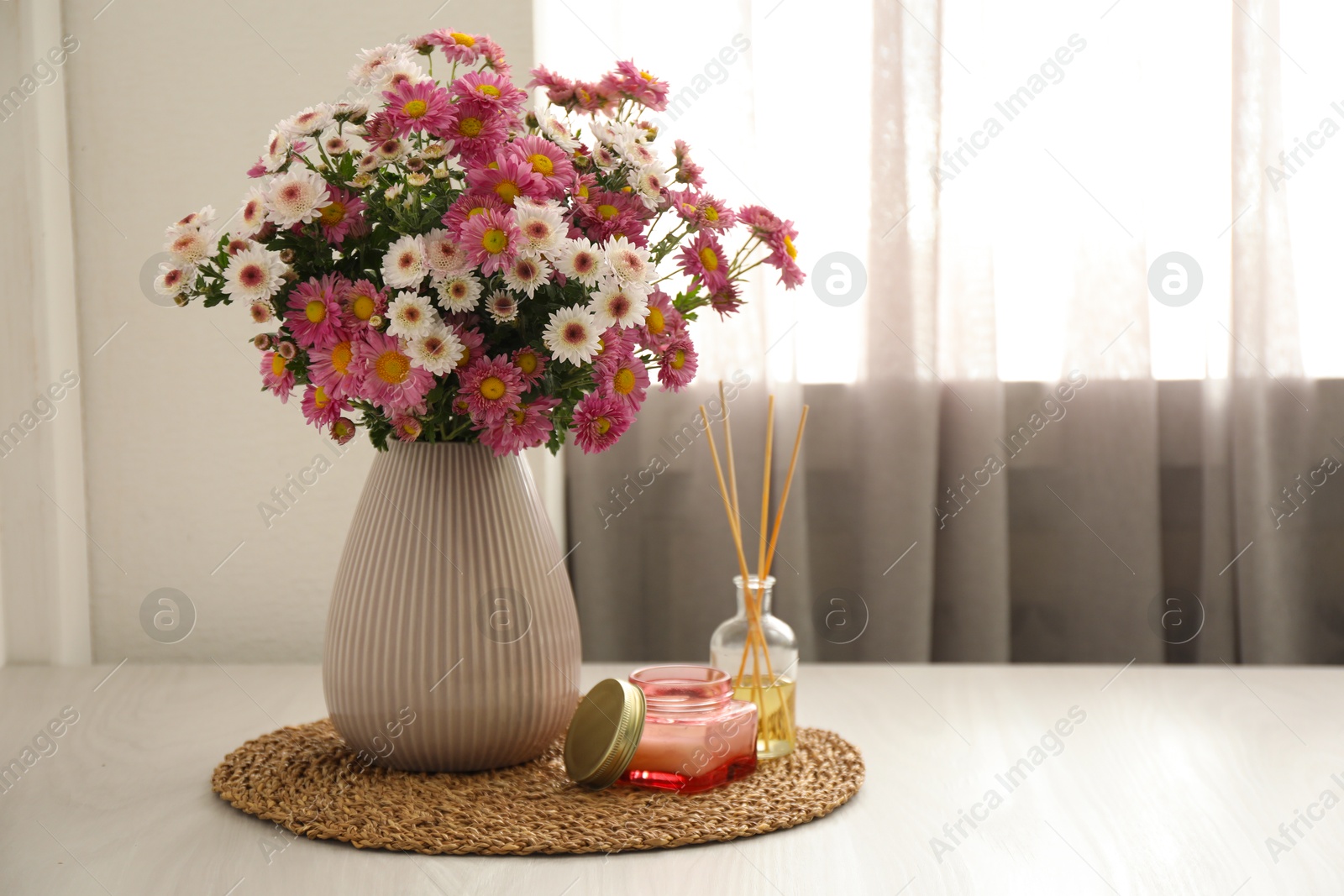 Photo of Beautiful flowers in vase, candle and reed diffuser on white wooden table at home, space for text