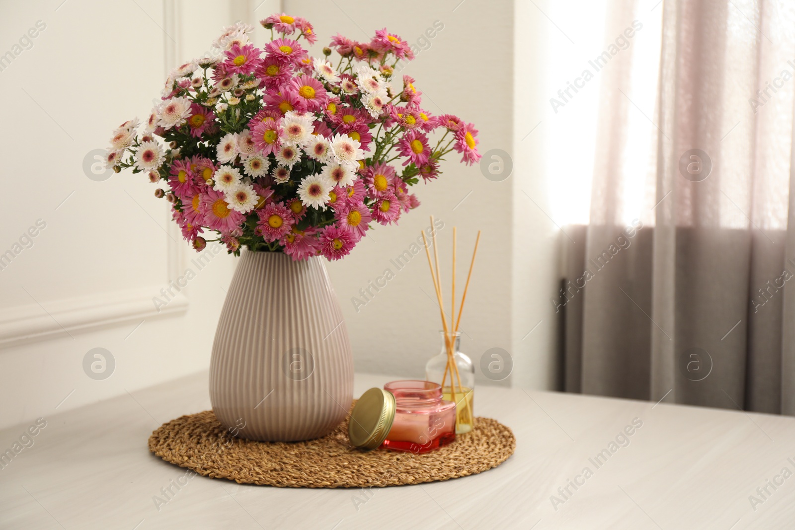 Photo of Beautiful flowers in vase, candle and reed diffuser on white wooden table at home, space for text