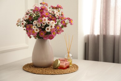 Photo of Beautiful flowers in vase, candle and reed diffuser on white wooden table at home, space for text