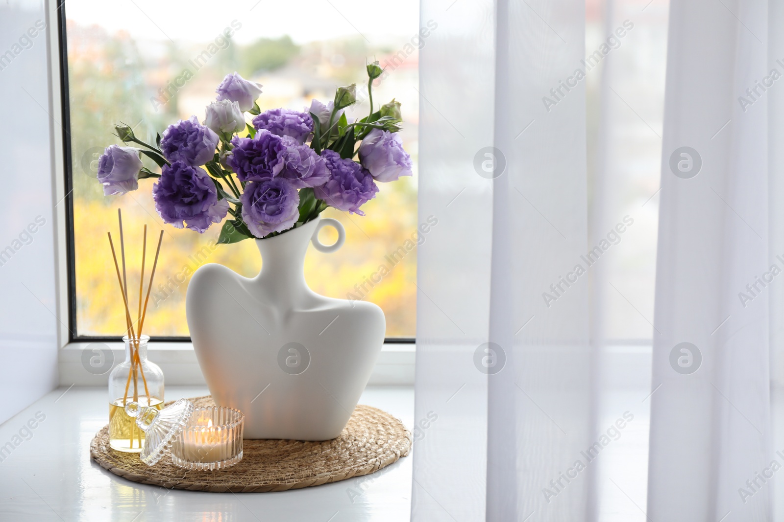 Photo of Stylish vase with beautiful flowers, candle and reed diffuser near window at home