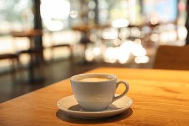 Photo of Cup of delicious coffee on wooden table in cafe