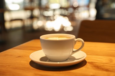 Photo of Cup of delicious coffee on wooden table in cafe