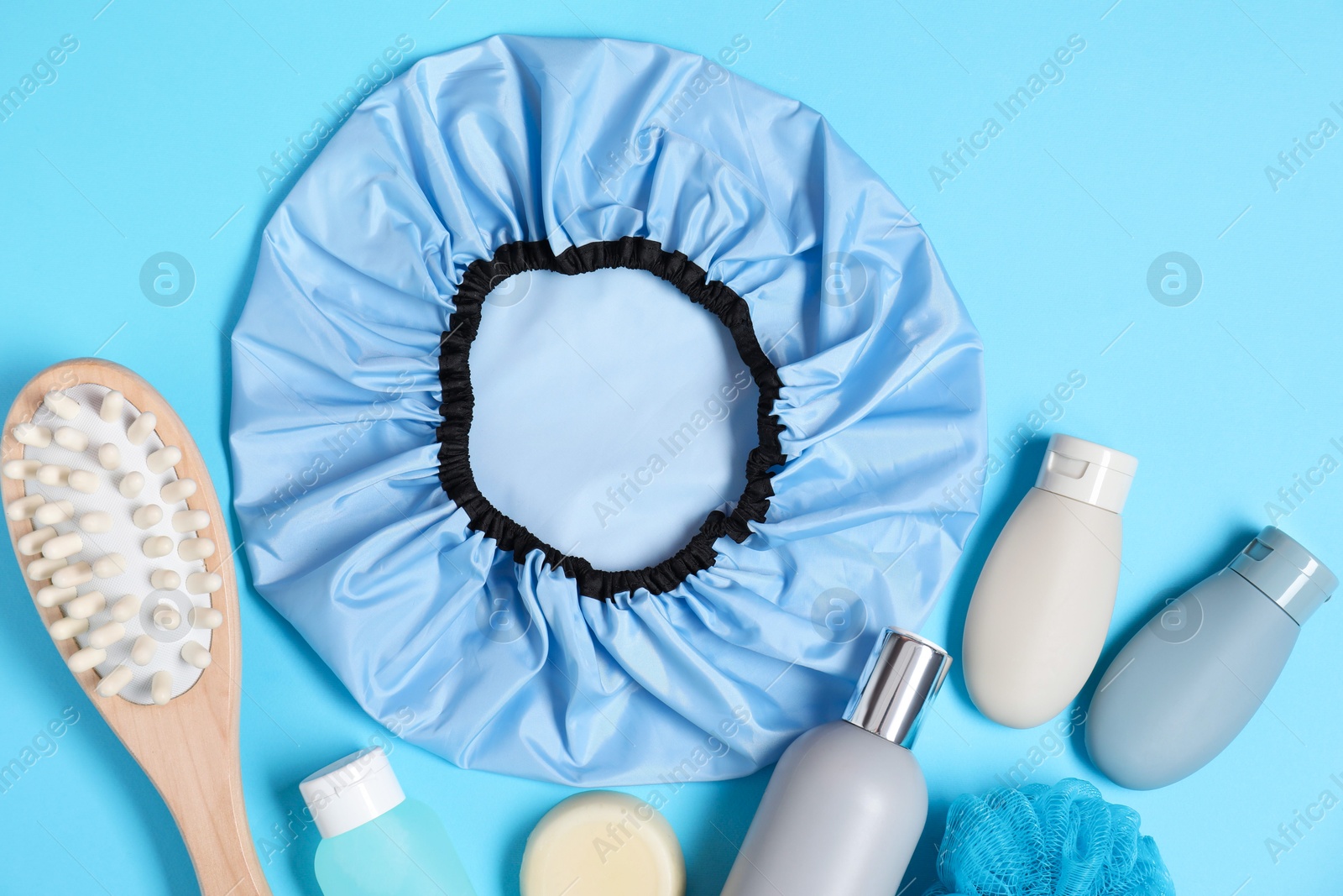 Photo of Shower cap and bath accessories on light blue background, flat lay