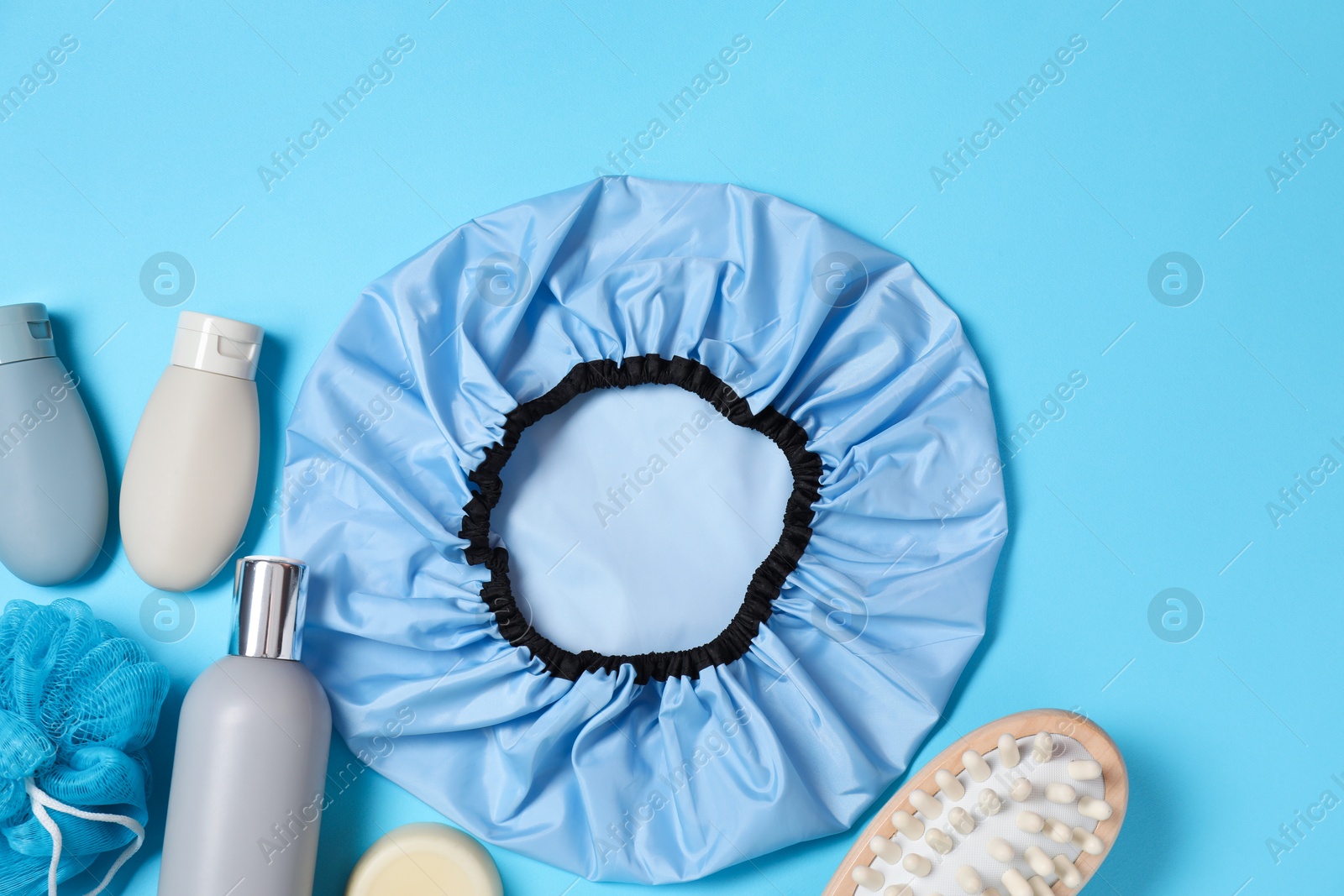 Photo of Shower cap and bath accessories on light blue background, flat lay