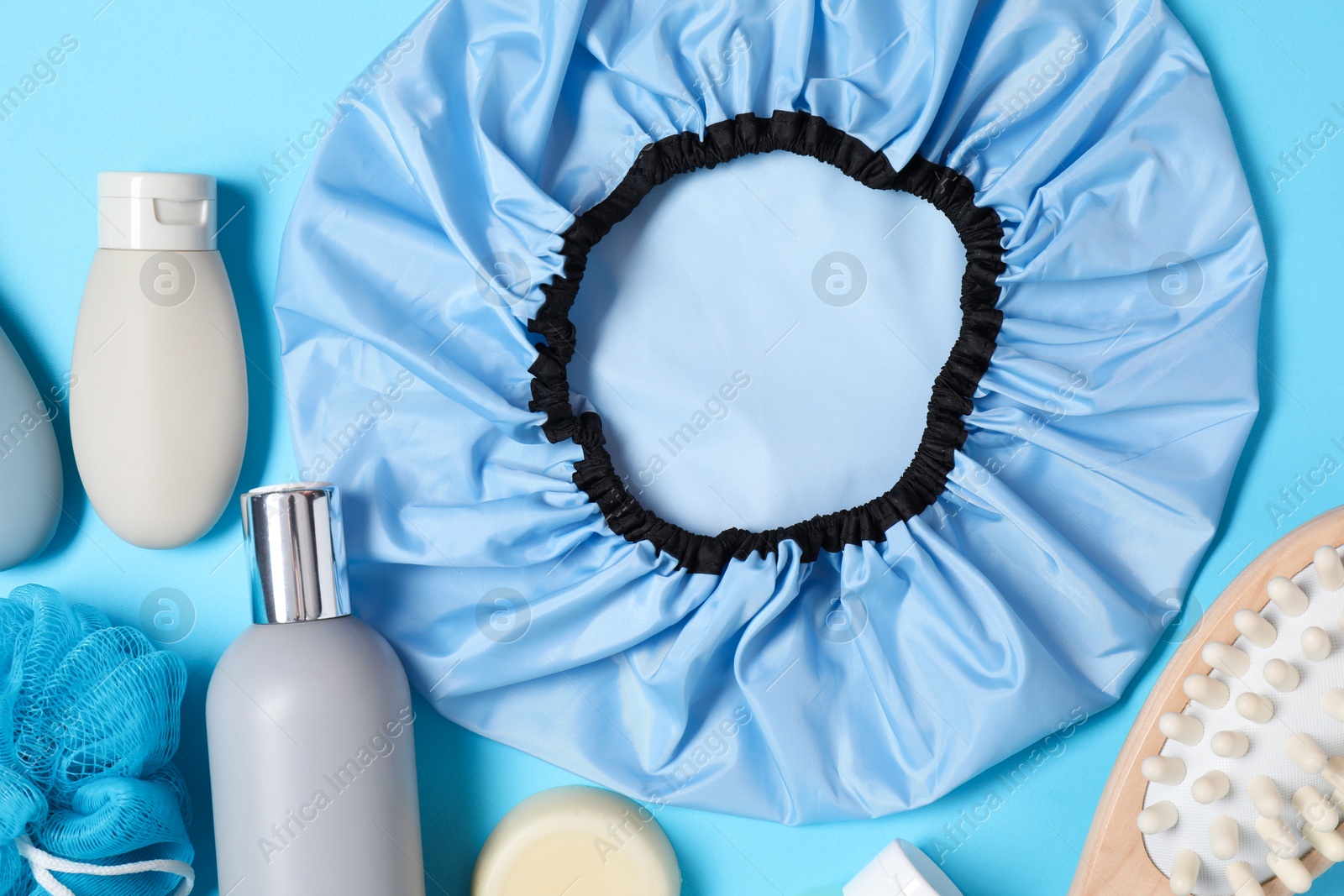 Photo of Shower cap and bath accessories on light blue background, flat lay