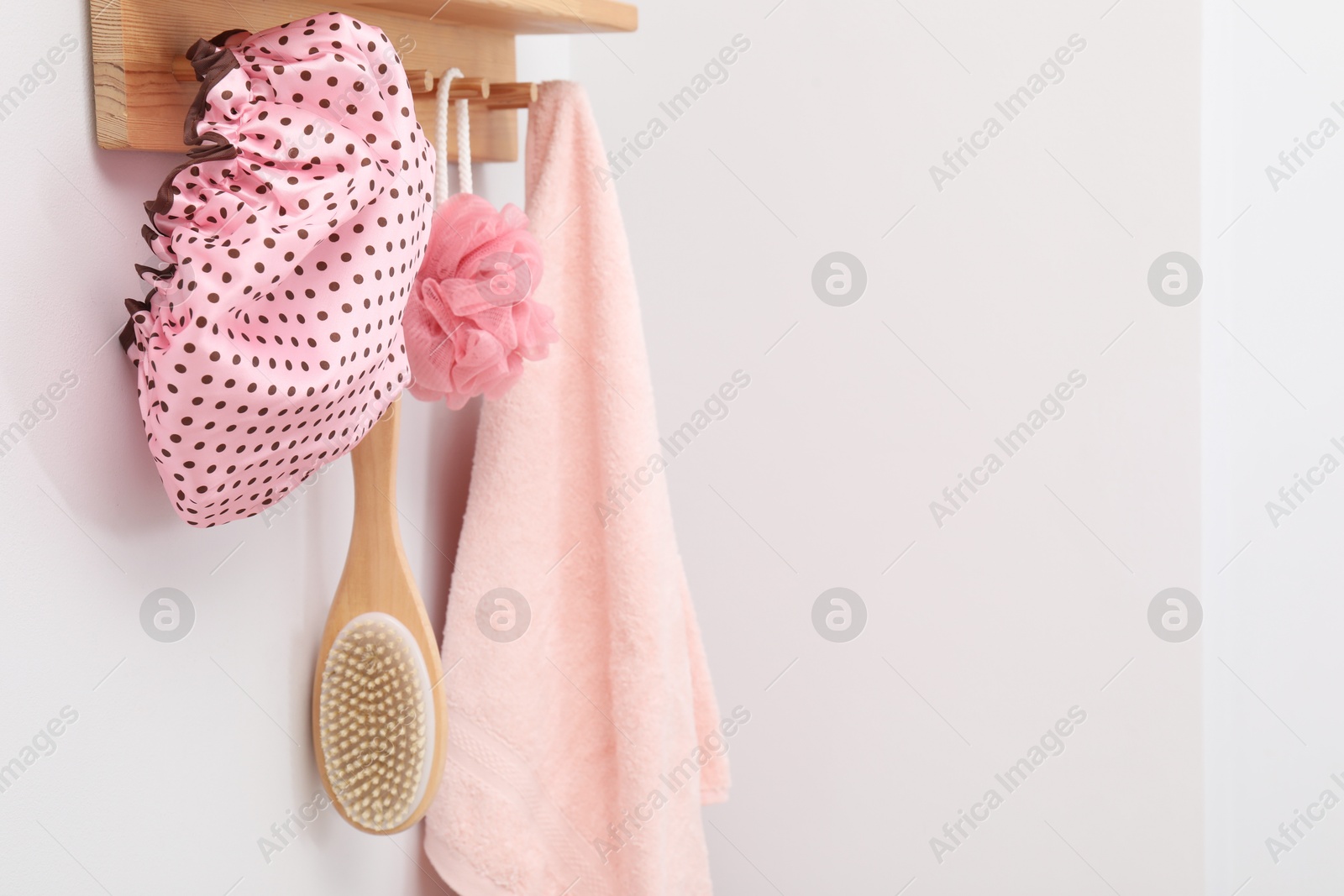 Photo of Shower cap, brush, mesh sponge and towel on rack indoors, space for text