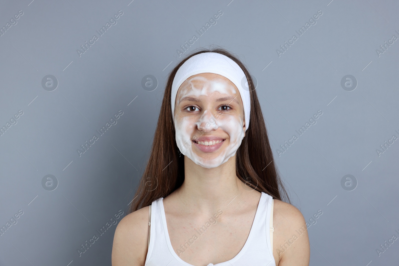 Photo of Teenage girl with cleansing foam on her face against grey background. Acne treatment