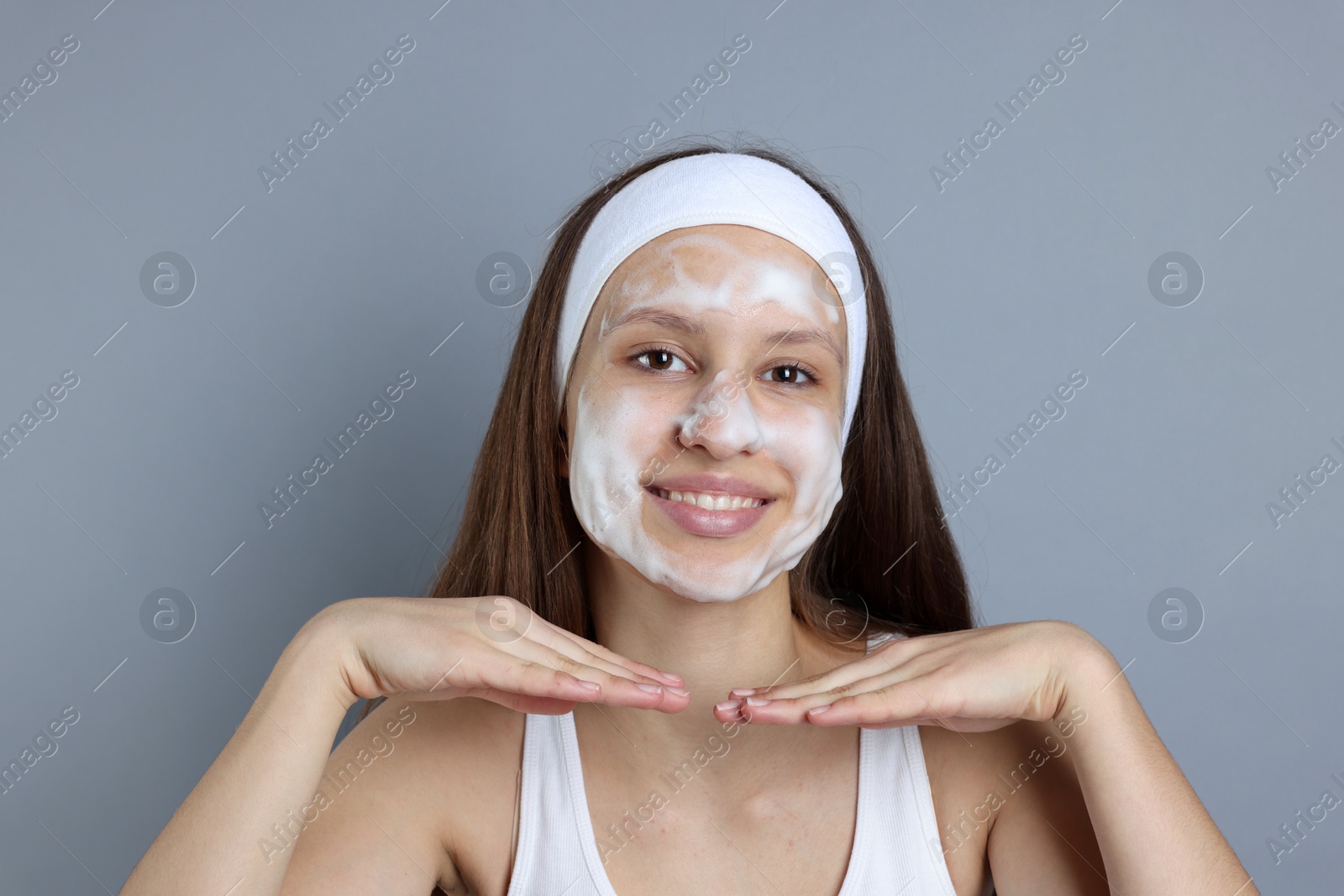 Photo of Teenage girl with cleansing foam on her face against grey background. Acne treatment